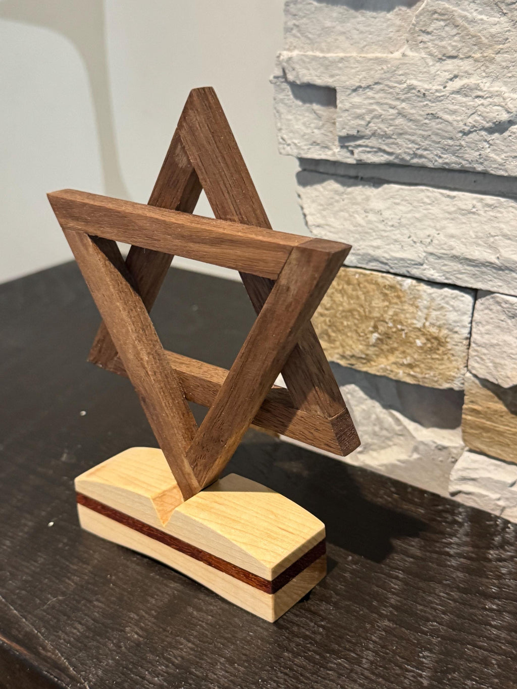 An angled three-quarter view of the wooden Magen David sculpture, beautifully showcasing the vibrant reddish-orange hues of the Padauk wood intertwined with darker walnut and lighter maple wood tones. __etsy:8156470266