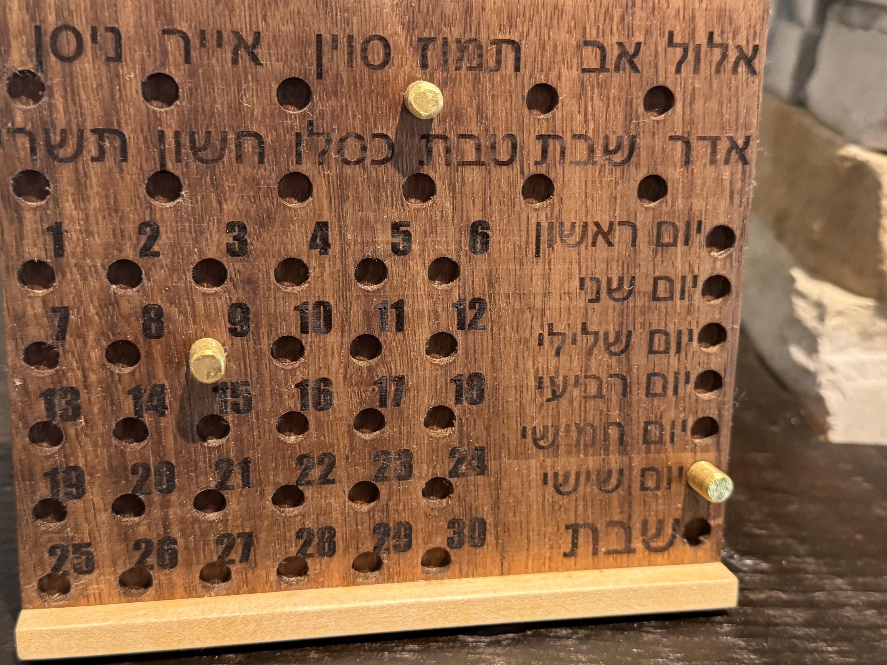 Close-up of a wooden Hebrew perpetual calendar detailing the engraved Hebrew text, numbered days, and bronze pins inserted into the tracking holes. __etsy:8156632656